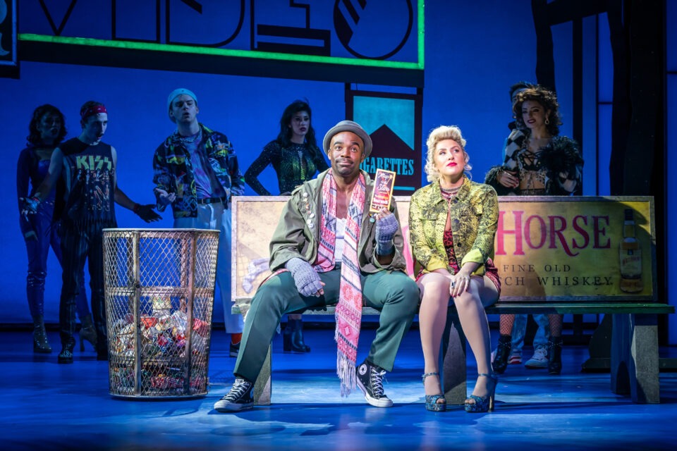 A man and a woman sit next to each other on a bench in Pretty Woman the Musical