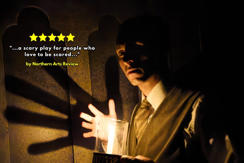 Man Holds a candle, casting an ominous shadow on the wall in The Woman in Black play
